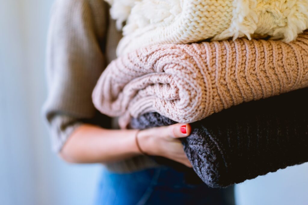 A woman holding folded sweaters.